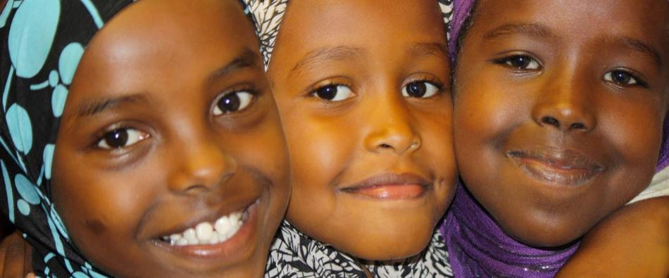 Three smiling refugee children representing the community RHR serves